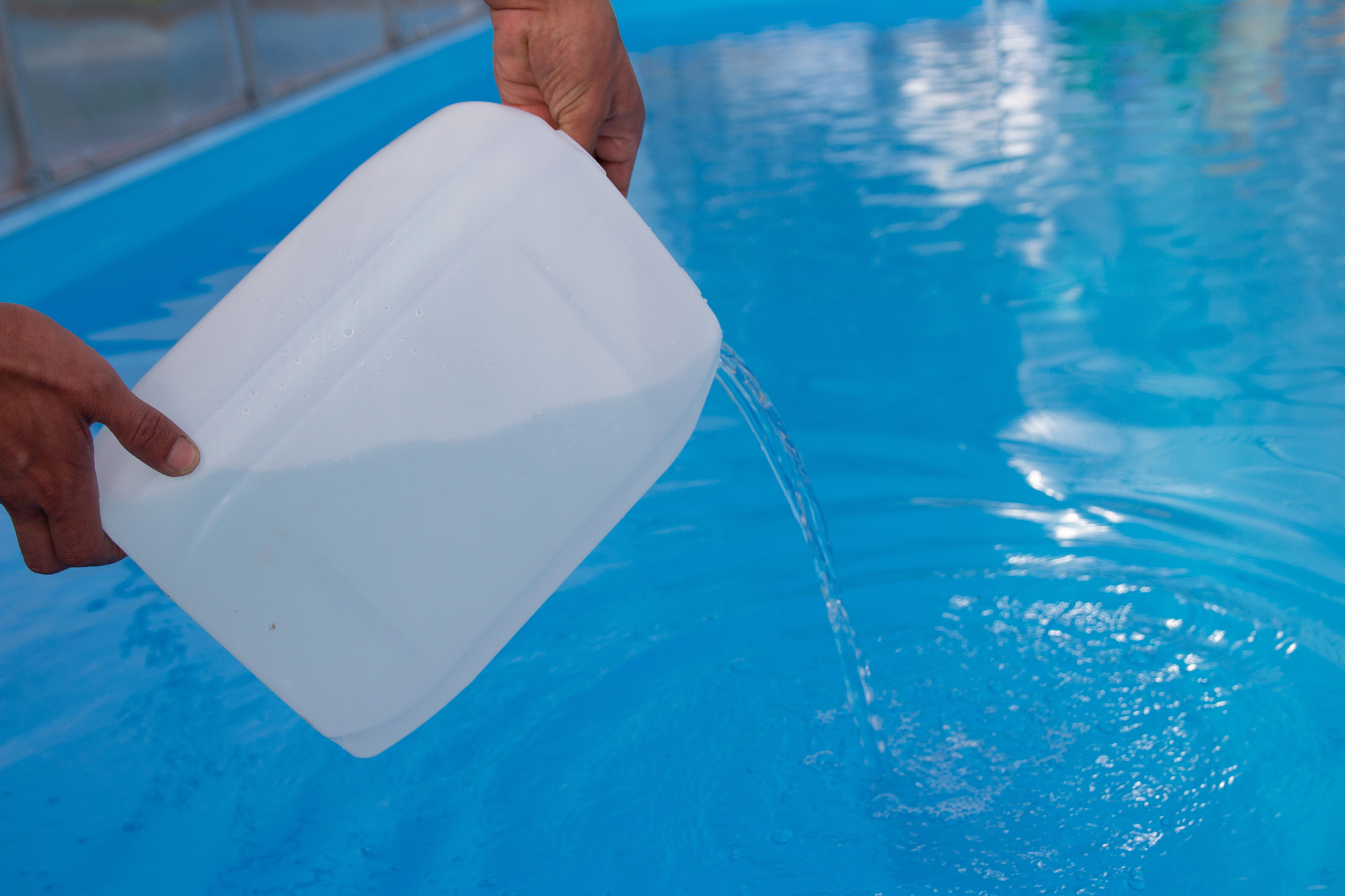 Image of men's hands pouring light liquid from a plastic tank into a pool, featuring Lonestar Pool Services and highlighting pool acid, ensuring it aligns with the page's context.